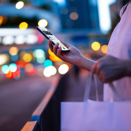 Woman on the street looking at her mobile phone while carrying a shopping bag
